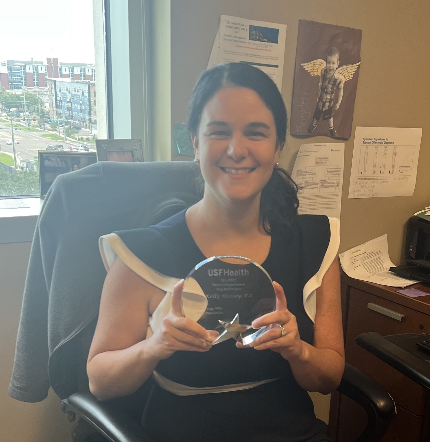 Kelly Hussey smiling holding a glass award wearing a black dress with white pipping