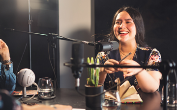 A woman speaking into a microphone during a podcast recording