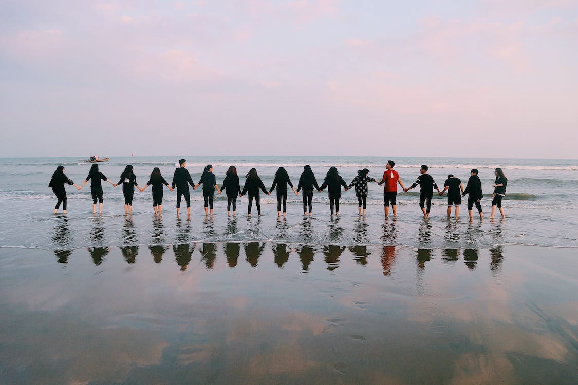 group of people in a line holding hands at the beach