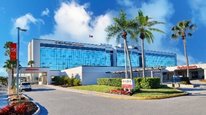 White building with large blue windows across the front with three tall palm trees planted in front
