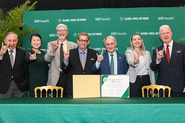 Dr. Gallow standing in the middle of a group of researchers, all with outreached arms using their hands to display the USF Bull symbol