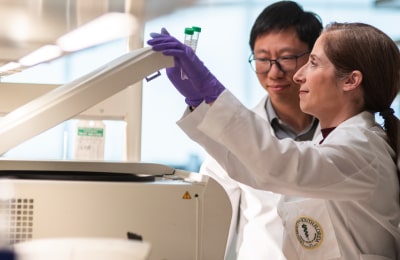 Two professionals in lab coats observing a machine, engaged in scientific analysis in a lab environment.