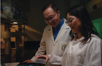 A man and woman in lab coats collaborate while examining lab samples in a laboratory setting.