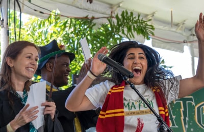An excited student cheering loudly in front of a microphone with their hands raised.