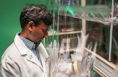 A man in a lab coat examines an object with a focused expression in a laboratory setting.