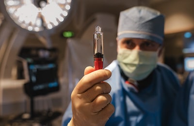 A surgeon in scrubs holds a syringe, preparing for a medical procedure in a clinical setting.